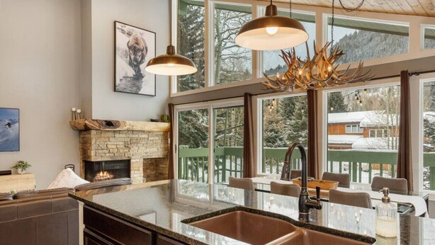 A modern kitchen with a stone fireplace, large windows, and a dining area with a view of a snowy landscape.