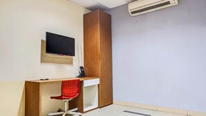 A room with a wooden desk, a red office chair, a flat-screen TV, and an air conditioning unit.