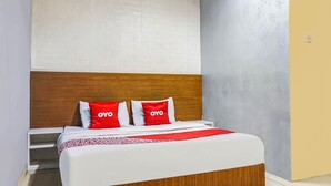 A hotel room with a wooden headboard, a white bedspread, and red pillows with the "OYO" logo.