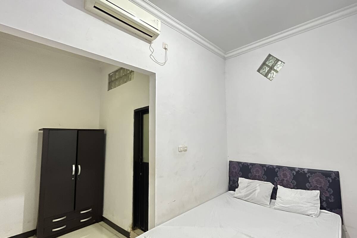 A bedroom with a bed, a wardrobe, an air conditioning unit, and a decorative wall piece.