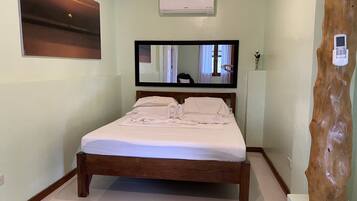 Un lit bien fait, avec une tête de lit en bois, un grand miroir au-dessus et un climatiseur fixé au mur.