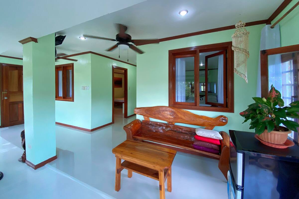 A room with a wooden bench, a small table, a ceiling fan, and a potted plant.