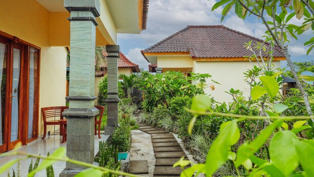 A courtyard with a tiled pathway, wooden chairs, and a stone pillar. - Salang Guest House (Penida Island)