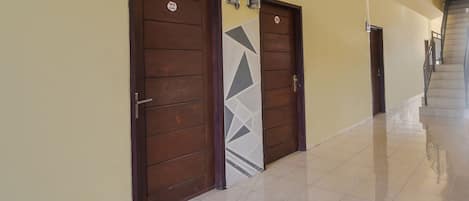 A hallway with two wooden doors, each marked with a number. The floor is tiled, and there is a staircase at the end of the hallway.