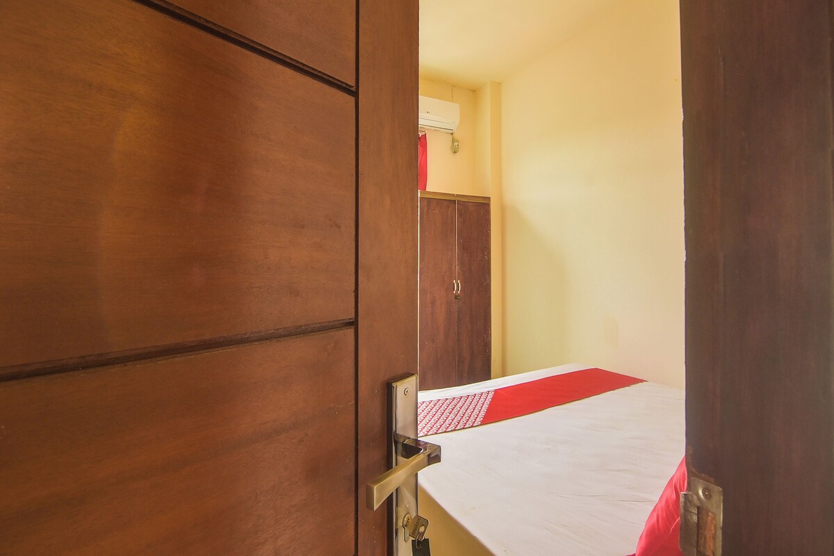 A room with a wooden wardrobe, a bed with a red and white bedspread, and a wall-mounted air conditioner.