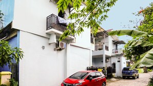A residential building with balconies, a red car parked in front, and a blue car parked further back. - OYO Life 92046 Garuda Residence (Palembang)