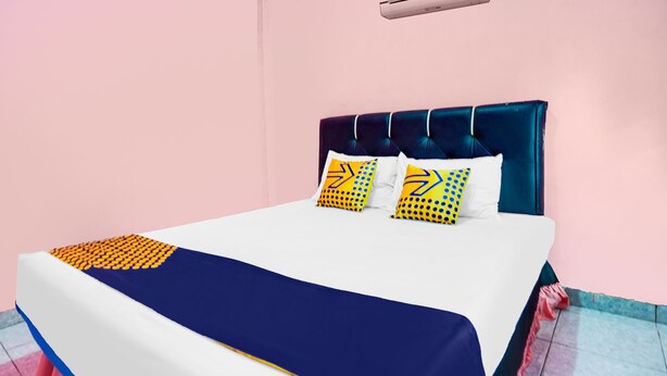 A bed with a blue headboard, white bedding, and two pillows with yellow and blue patterns. - OYO Life 92046 Garuda Residence (Palembang)
