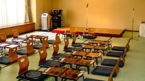 Un salón de conferencias con mesas y sillas en fila, un escenario con alfombra roja y un atril.