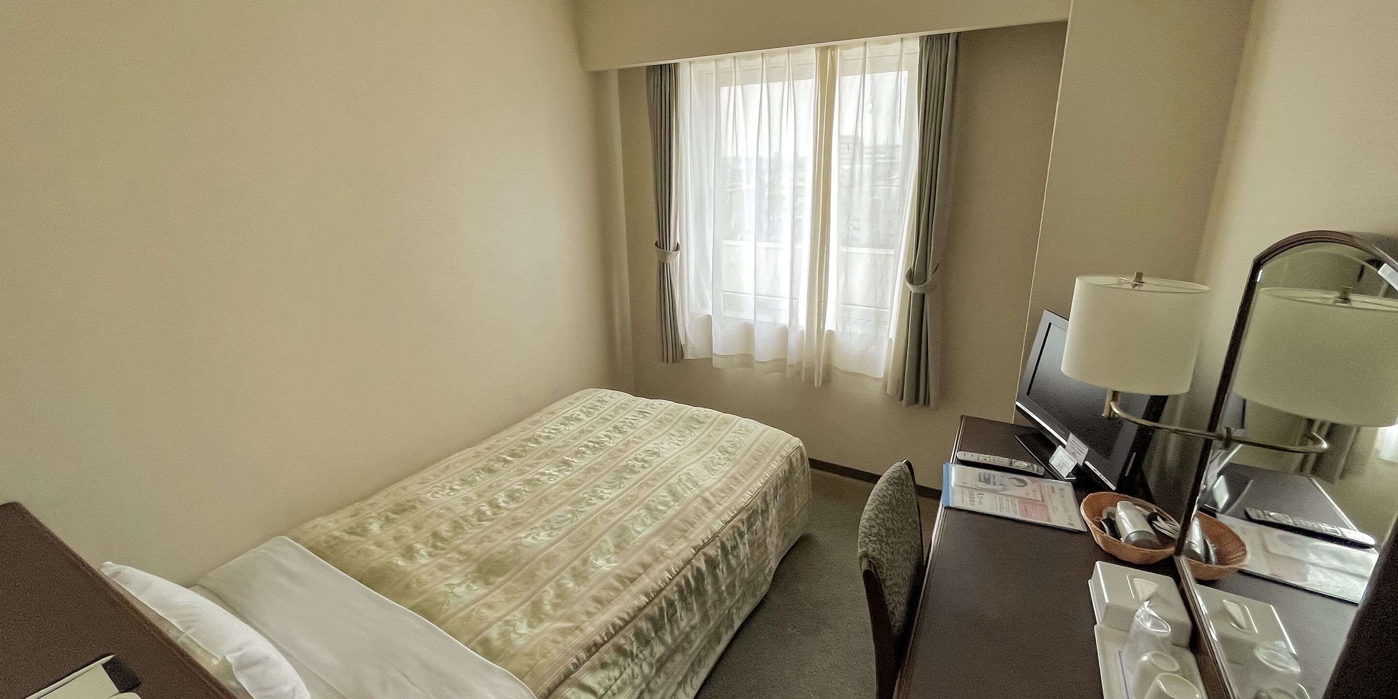 Ein Hotelzimmer mit Bett, Schreibtisch mit Lampe, Stuhl und einem Fenster mit Vorhängen.