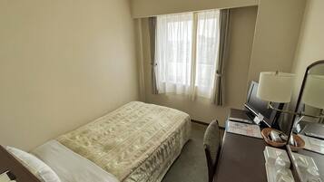 Ein Hotelzimmer mit Bett, Schreibtisch mit Lampe, Stuhl und einem Fenster mit Vorhängen.