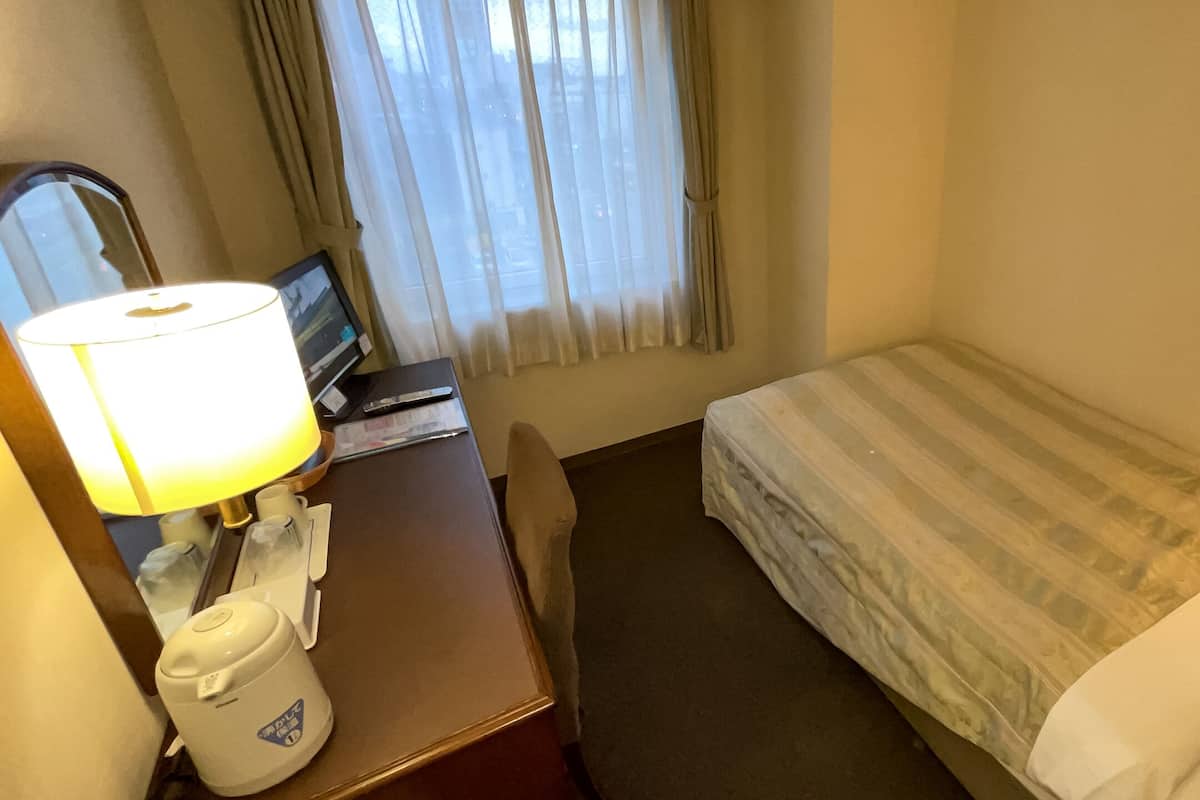 Una habitación de hotel con cama, escritorio con lámpara, teléfono y ventana con cortinas.