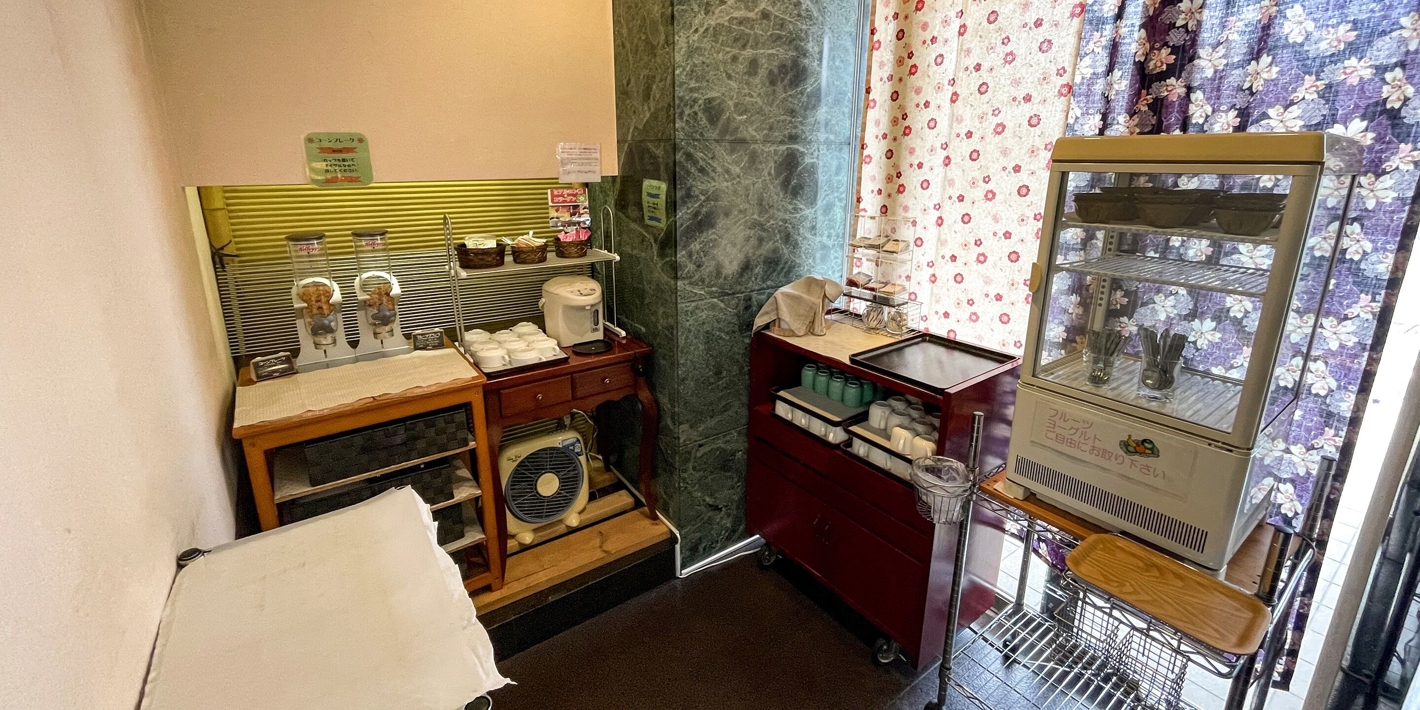 A small kitchenette with a coffee maker, a fan, and a microwave. There is a small shelf with condiments and a basket.