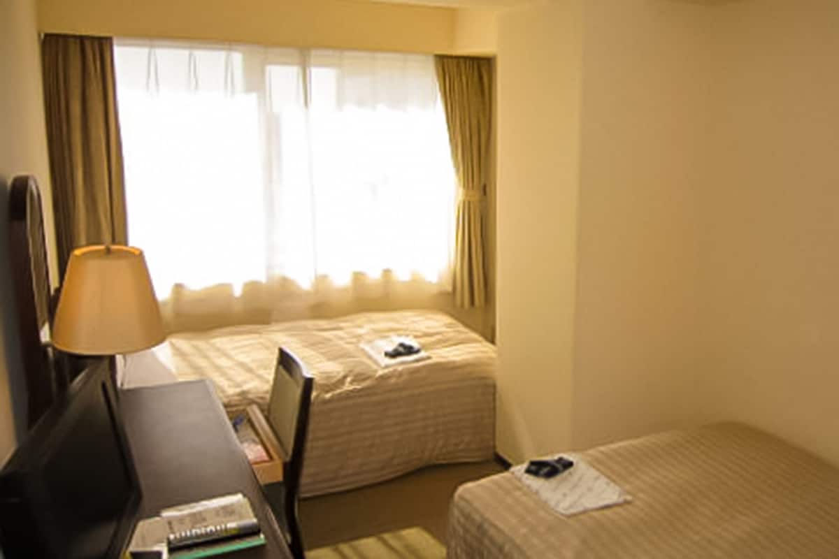 Habitación de hotel con dos camas, un escritorio y una lámpara.