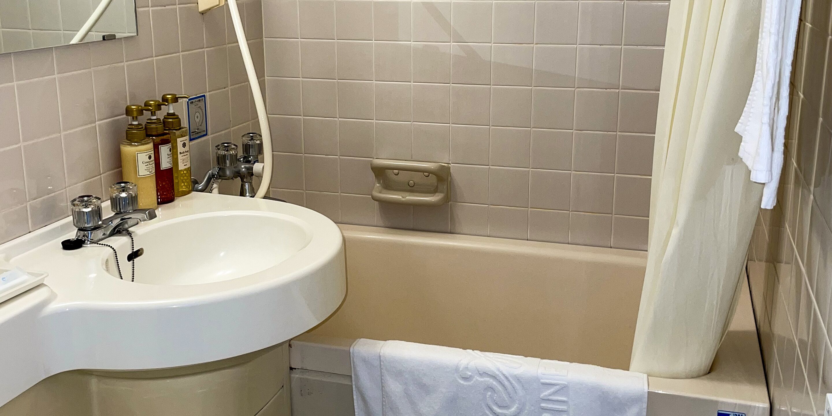 A bathroom with a white sink, a bathtub, and a mirror. There are toiletries on the sink and a towel hanging on the wall.