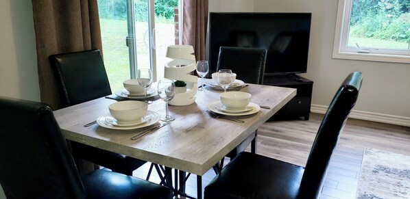 A dining area with a wooden table set for four, black chairs, a television, and a view of greenery outside. - Cheerful 2 Bdrm house, free Netflix, free parking for 2 cars (Kitchener)