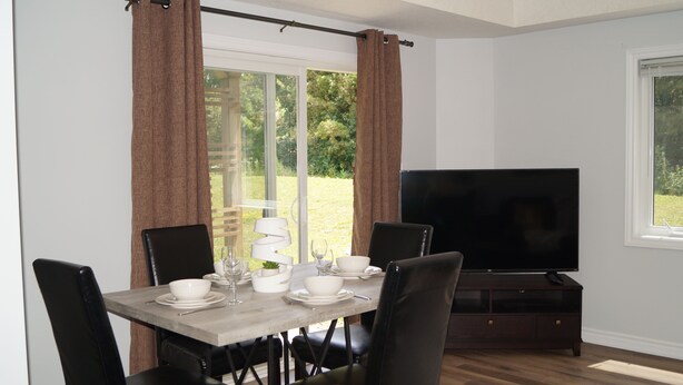 Un coin repas avec une table dressée pour quatre personnes, un téléviseur et une vue sur l’extérieur.