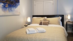 Un lit bien fait, avec une literie à motifs, deux lampes de chevet et une serviette pliée posée sur le lit.