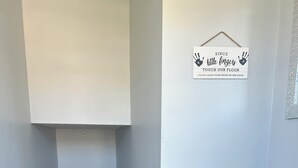 Un couloir avec un sol carrelé, un banc, une porte et un panneau sur le mur.
