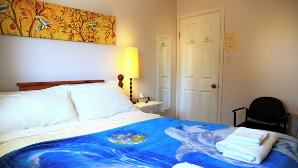 Una habitación de hotel con una cama, una mesita de noche, una silla y un cuadro en la pared.