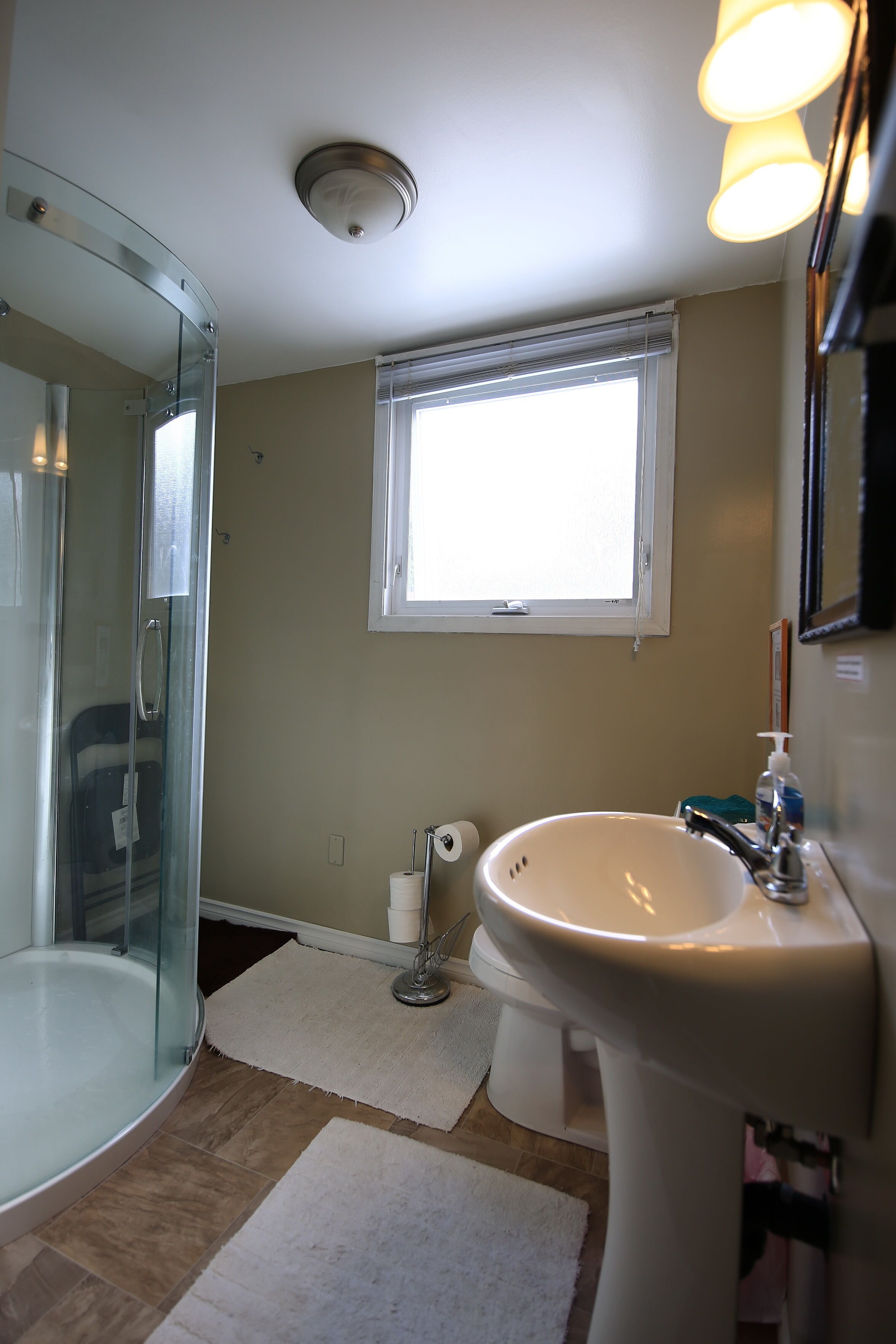 A bathroom with a glass shower enclosure, a sink, a toilet, and a window providing natural light.