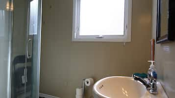 A bathroom with a glass shower enclosure, a sink, a toilet, and a window providing natural light.