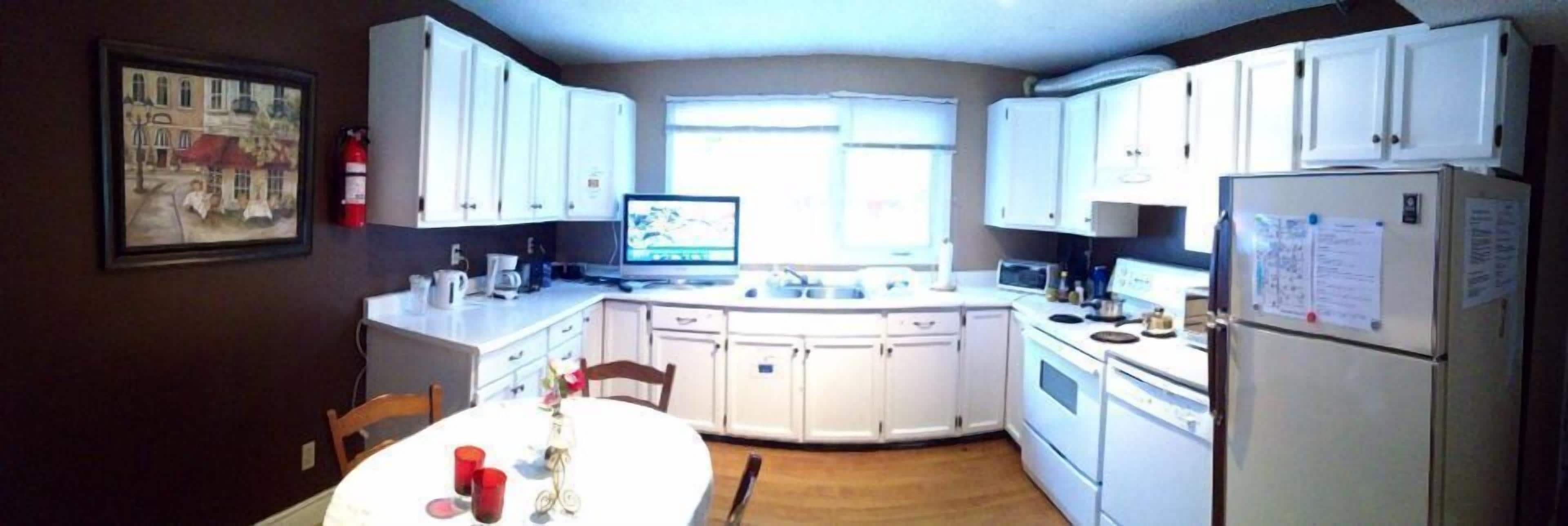 Una cocina compacta con armarios blancos, una mesa de comedor con tazas rojas y una ventana que deja entrar luz natural.