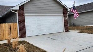 Un garage attenant à une maison, avec une porte de garage blanche, une façade en briques et un drapeau américain.