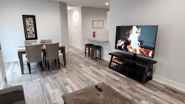 Un salon moderne avec un plancher en bois, un coin repas comprenant une table et des chaises, un téléviseur à écran plat fixé au mur et une petite table basse.