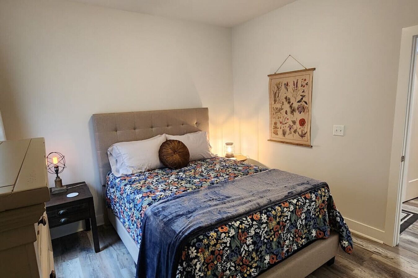 Une chambre à coucher comprenant un lit, une table de chevet, une lampe et une œuvre d’art accrochée au mur.