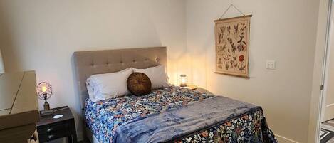 Une chambre à coucher comprenant un lit, une table de chevet, une lampe et une œuvre d’art accrochée au mur.