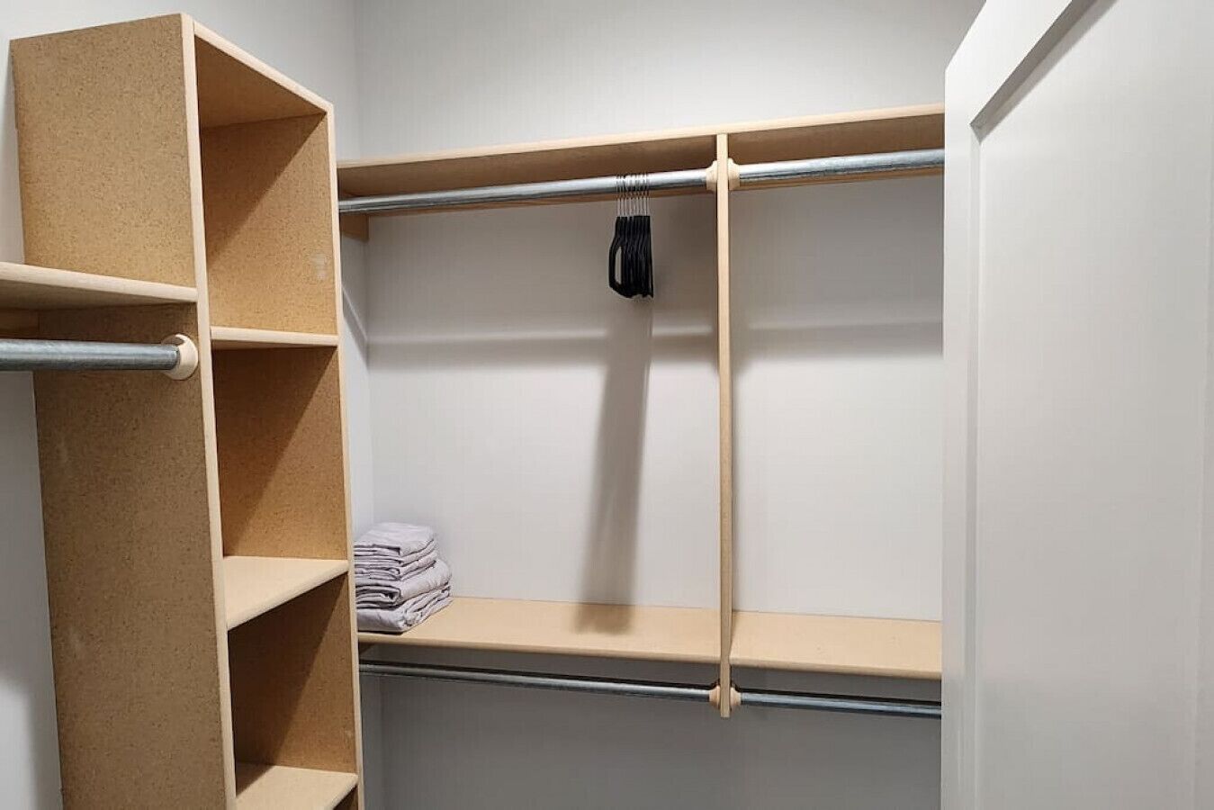 Un placard avec des étagères ouvertes, une tringle pour suspendre les vêtements et une serviette pliée sur l’étagère du bas.