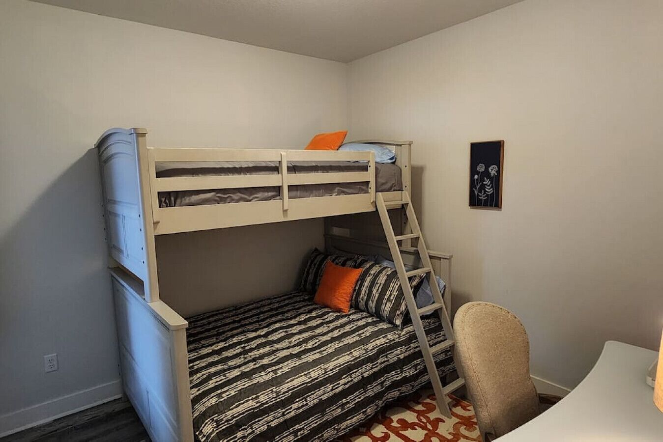 Una cama litera con una escalera, una silla y un cuadro en la pared.