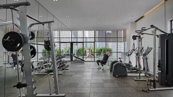 Un gimnasio moderno con diversos equipos de ejercicio, ventanas amplias y vistas a edificios de la ciudad.