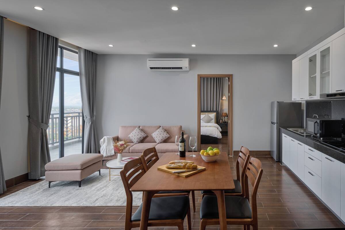 A modern hotel room with a dining area, kitchenette, and a balcony with curtains.