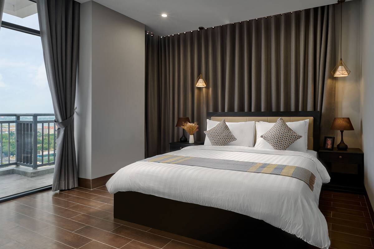 A modern bedroom with a large bed, dark curtains, and two bedside lamps.