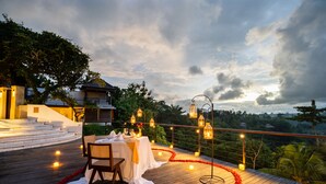 A wooden deck with a table set for two, surrounded by candles and lanterns, overlooking a lush landscape. - Uma Kalai (Ubud)