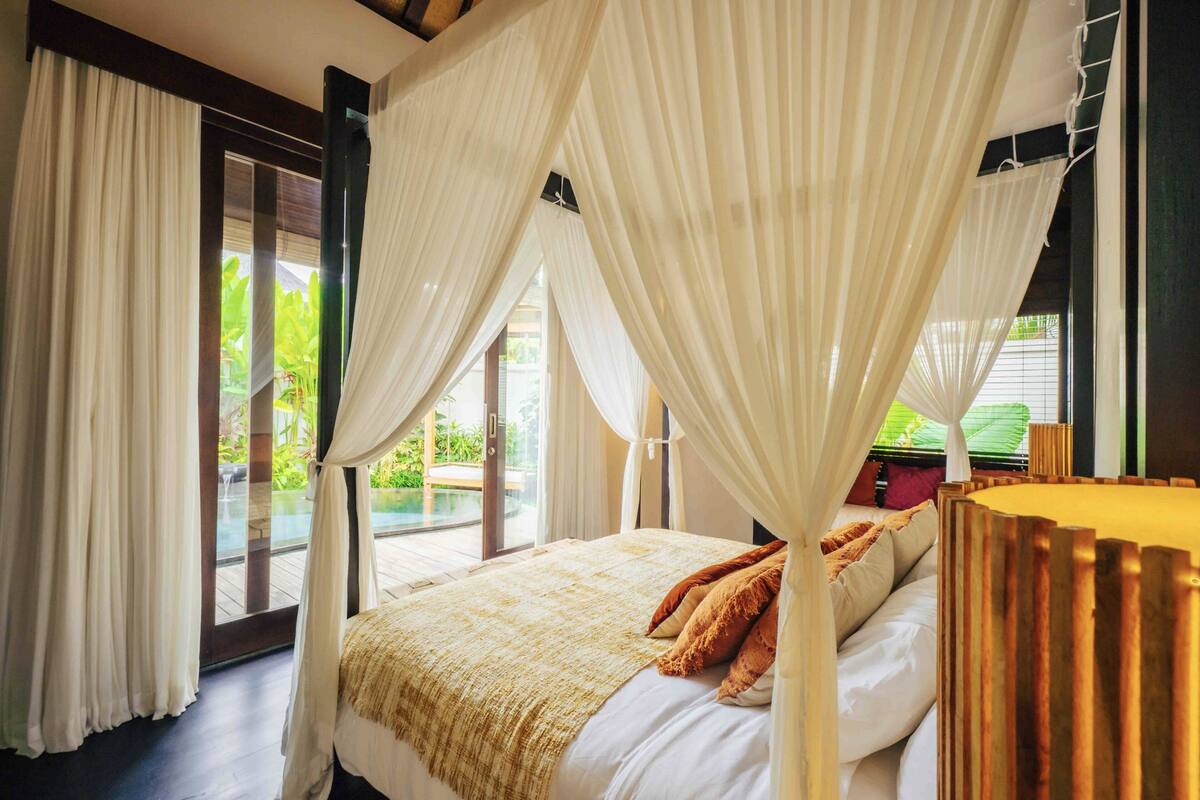 A bedroom with a bed, curtains, and a view of greenery outside.