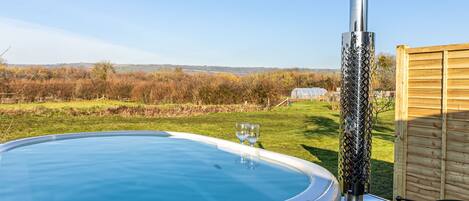 Een hottub met uitzicht op het omliggende landschap, een houten omheining en een barbecue.