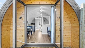 Un intérieur chaleureux et en bois, dans une petite structure semi-ouverte comprenant un coin cuisine, une table à manger et un espace salon.