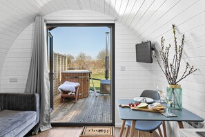 A cozy interior with a wooden hot tub, a dining table set with food and drinks, and a view of the outdoors.