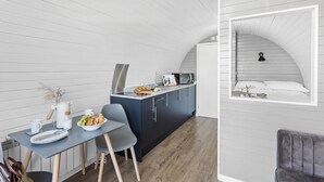 A compact kitchen with a dining area, a built-in stove, and a small dining table with chairs. - Windsor Glamping Pod- Free Wi-Fi, Hot Tub (Wells)