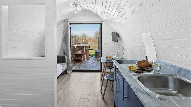 A compact, modern kitchen with a sink, a dining area with a table and chairs, and a view of the outdoors. - Windsor Glamping Pod- Free Wi-Fi, Hot Tub (Wells)