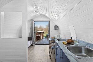 A compact, modern kitchen with a sink, a dining area with a table and chairs, and a view of the outdoors. - Windsor Glamping Pod- Free Wi-Fi, Hot Tub (Wells)