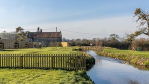 A rural landscape with a river, a wooden fence, and a stone building with a tiled roof. - Windsor Glamping Pod- Free Wi-Fi, Hot Tub (Wells)