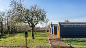 A row of modern, dark-colored, arched buildings with a gravel path leading to a wooden signpost. - Morgan Sweet Glamping Pod - Free Wi-Fi (Wells)