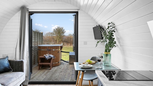 A cozy interior with a wooden hot tub, a dining area with a table and chairs, and a sofa. - Morgan Sweet Glamping Pod - Free Wi-Fi (Wells)