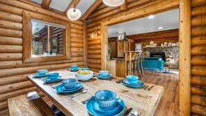 A wooden cabin interior with a dining table set for four, a kitchen area, and a large window.