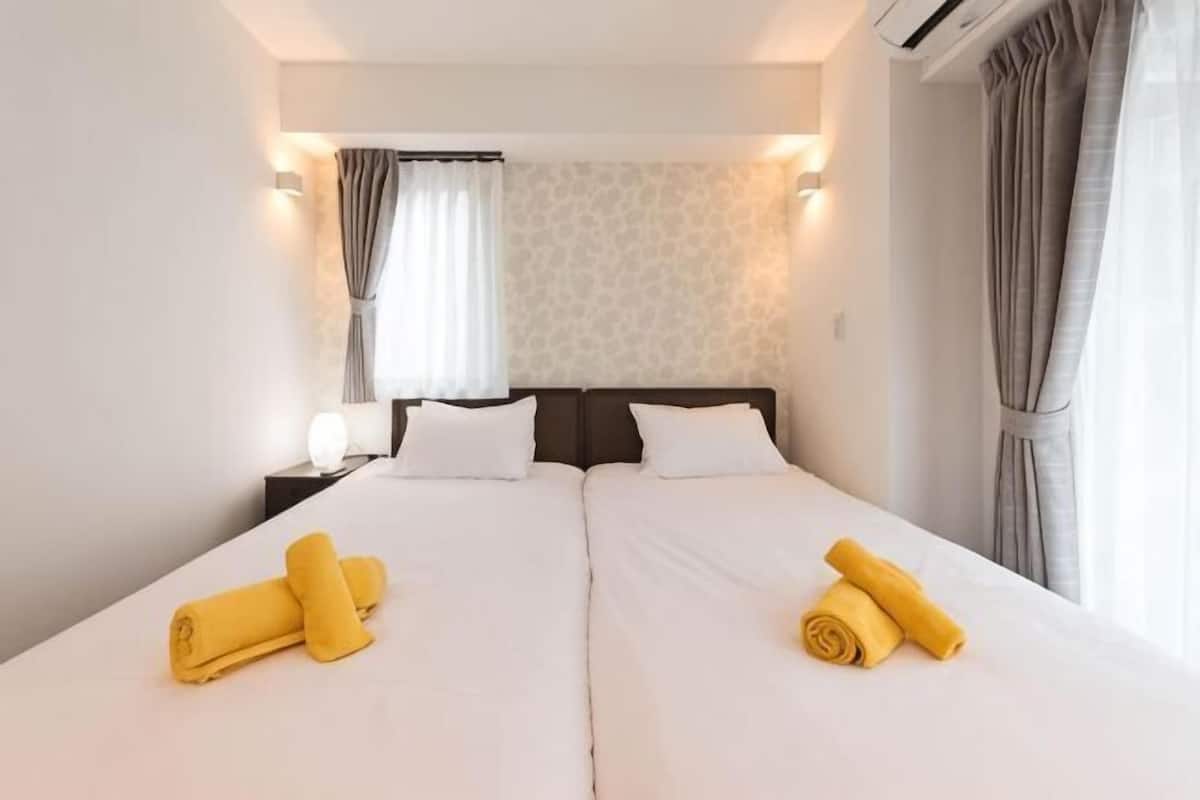 A double bed with white linens, two pillows, and two rolled towels.