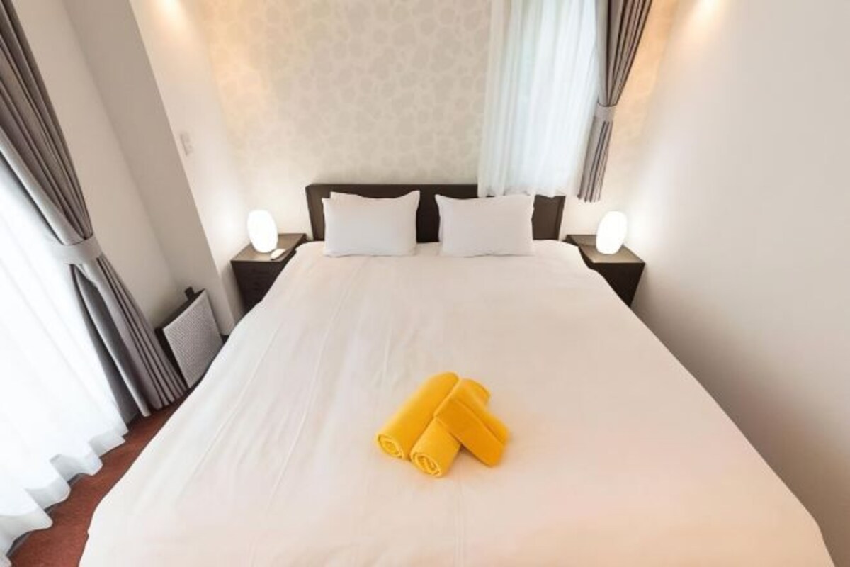 A hotel room with a large bed, two bedside tables with lamps, and a curtain on the window.