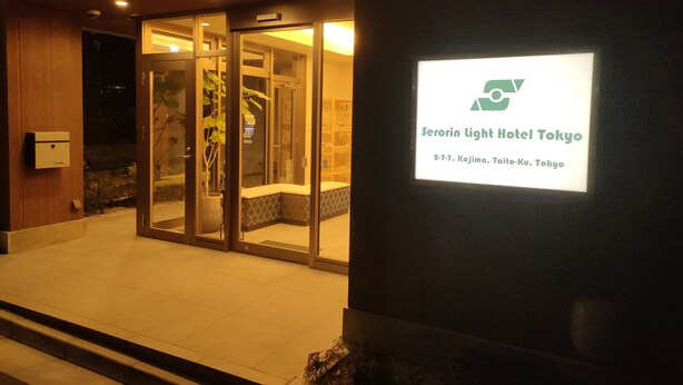 The exterior of Serorin Light Hotel Tokyo with a glass entrance, a mailbox, and a signboard displaying the hotel name and address. - Serorin Light Hotel Tokyo (Tokyo)